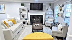 A living room with a white sofa, yellow ottoman, and a fireplace. - The Red Magnolia, Refreshing, Cozy, Game Room, Historic Roswell! (Roswell)