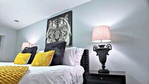 A bedroom with a bed, a nightstand, a lamp, and a tiger artwork on the wall. - The Red Magnolia, Refreshing, Cozy, Game Room, Historic Roswell! (Roswell)