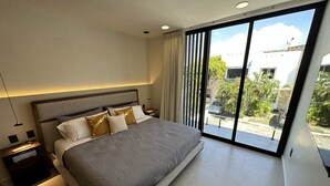 Una camera da letto moderna con un letto grande, un comodino, una lampada e vista sull'esterno attraverso ampie finestre.