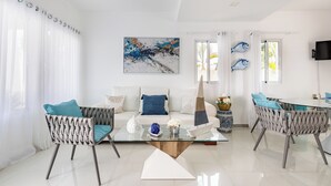 A modern living room with a glass coffee table, two wicker chairs, a sofa, and a dining table with chairs. There is a painting on the wall and a television mounted on the wall. - Private villa with pool, enjoy the Dominican Caribbean. (Cabarete)