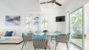 A modern living room with a white sofa, a glass dining table, wicker chairs, a ceiling fan, and a large window with curtains. - Private villa with pool, enjoy the Dominican Caribbean. (Cabarete)