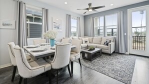 A modern living room with a dining area, large windows, and a ceiling fan. - Silver Strand Beach Bungalow (Imperial Beach)