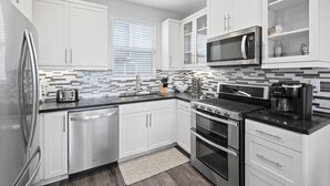 A modern kitchen with white cabinets, a stainless steel refrigerator, a microwave, a coffee maker, and a dishwasher. - Silver Strand Beach Bungalow (Imperial Beach)