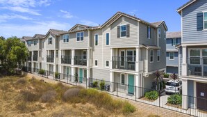 A row of townhouses with balconies, a paved driveway, and a fenced area with shrubs. - Silver Strand Beach Bungalow (Imperial Beach)