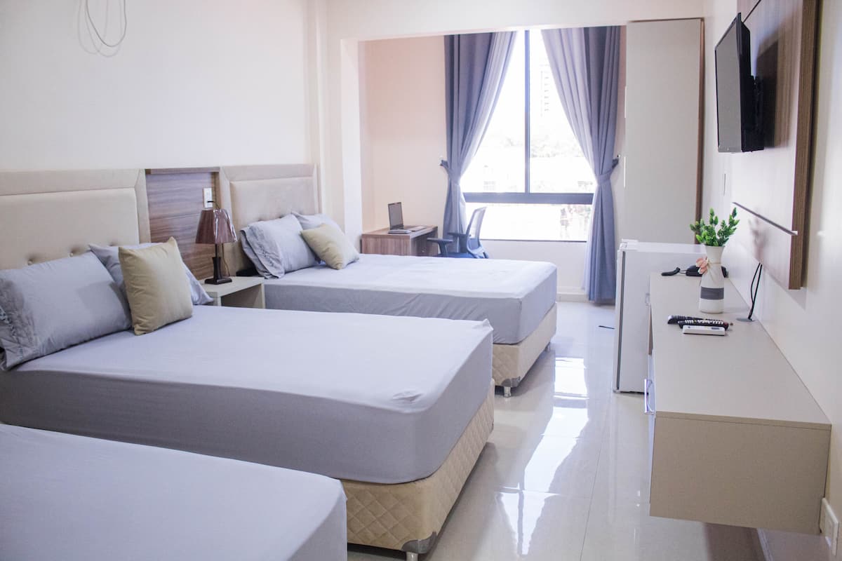 A hotel room with two beds, a desk, a TV, and a window with curtains.