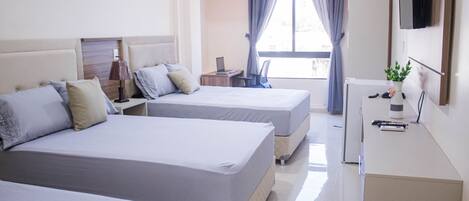 A hotel room with two beds, a desk, a TV, and a window with curtains.