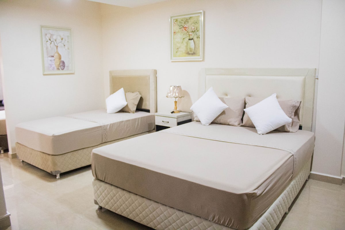 A hotel room with two beds, each with a headboard, a bedside table with a lamp, and artwork on the walls.