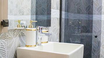 A bathroom with a large mirror, a white sink with gold fixtures, and patterned wallpaper.