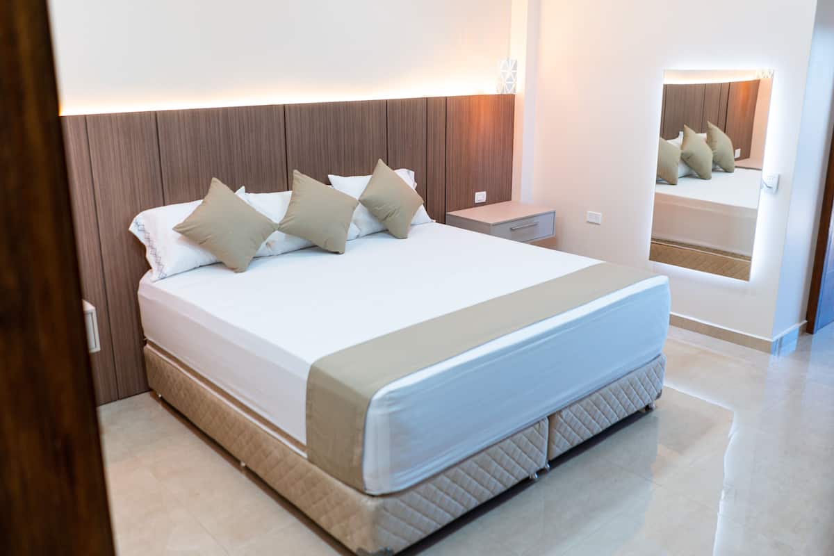 A modern bedroom with a large bed, a nightstand, a bedside table, and a mirror.