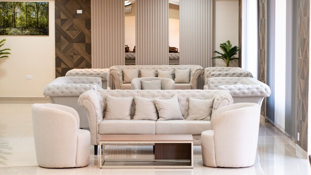 Un salon moderne avec un canapé central, deux fauteuils et une table basse. On y trouve des colonnes verticales et une grande fenêtre offrant une belle vue.