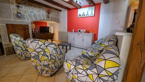 A living room with a stone fireplace, a red accent wall, and a sofa with a geometric pattern. - Gîtes de France 6 people in Le Teil (ALBARET LE COMTAL)