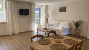En moderne stue med et tr æspisebord, hvid sofa og et fjernsyn ophængt på væggen.