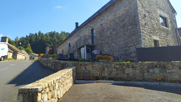Un bâtiment en pierre avec un toit en pente, un petit balcon et un mur de pierre à l’avant.