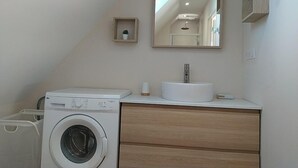 Une petite salle de bain équipée d’un lave-linge, d’un lavabo et d’un miroir.