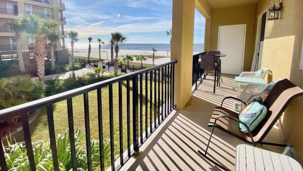 A balcony with a view of the beach, a table with chairs, and a door. - #113 Beautiful 2 bed 2 bath condo with beach views (Pass Christian)