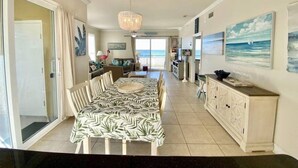 A spacious dining area with a large table, chairs, and a view of the ocean through the sliding glass door. - #113 Beautiful 2 bed 2 bath condo with beach views (Pass Christian)
