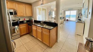 A modern kitchen with wooden cabinets, a black countertop, and a stainless steel refrigerator. - #113 Beautiful 2 bed 2 bath condo with beach views (Pass Christian)