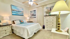 A bedroom with a bed, nightstands, a dresser, a ceiling fan, and wall art. - #113 Beautiful 2 bed 2 bath condo with beach views (Pass Christian)
