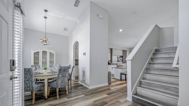 A modern kitchen with white cabinets, a dining area with a round table and patterned chairs, and a staircase with wooden steps.