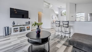 A modern living room with a flat-screen TV, a round black table with a vase, and a grey sofa.