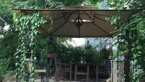Un área de estar al aire libre techada, con suelo de piedra y una pérgola cubierta de plantas trepadoras.