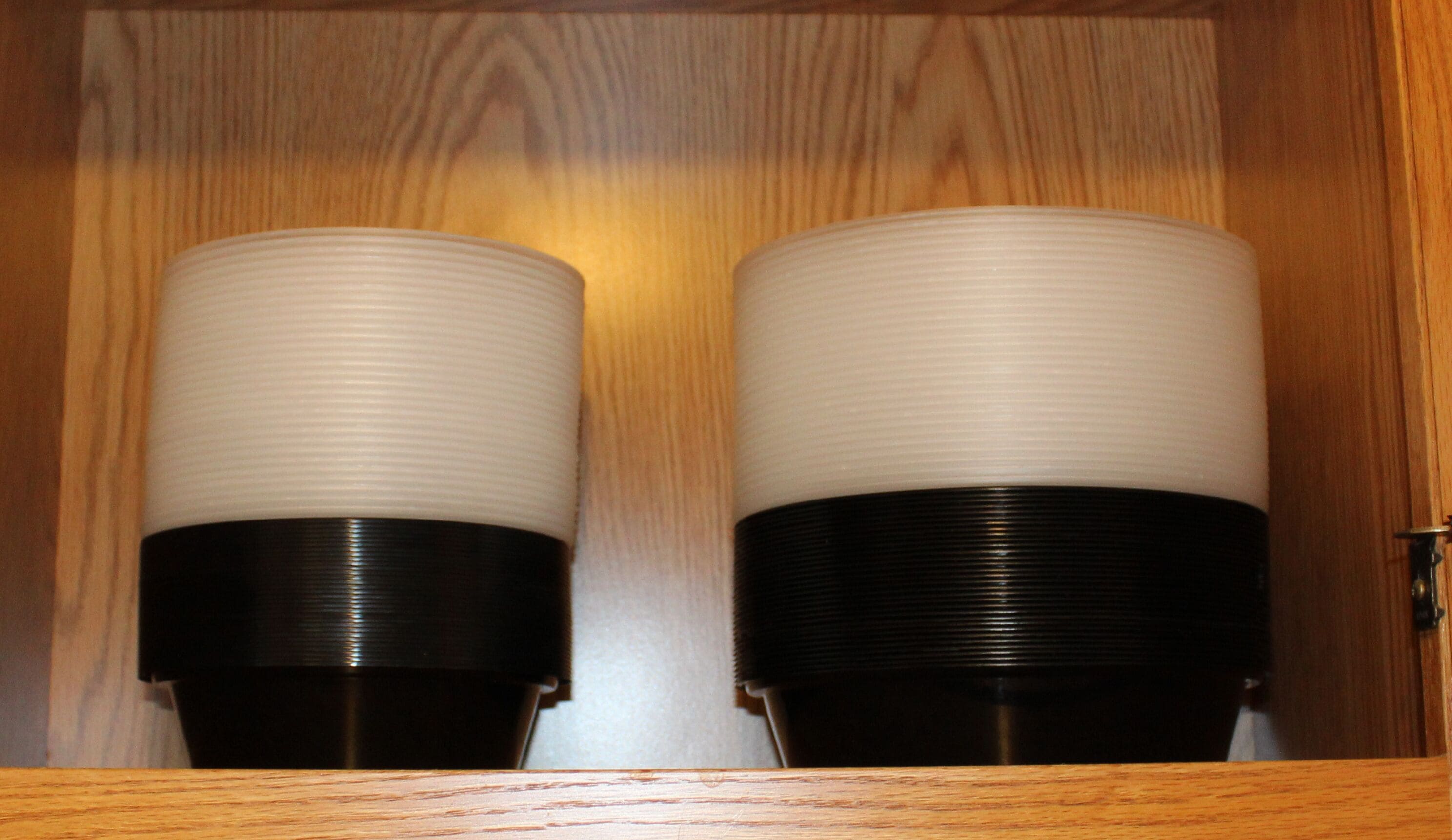 Dos objetos cilíndricos con textura acanalada, colocados uno al lado del otro en un mueble de madera.
