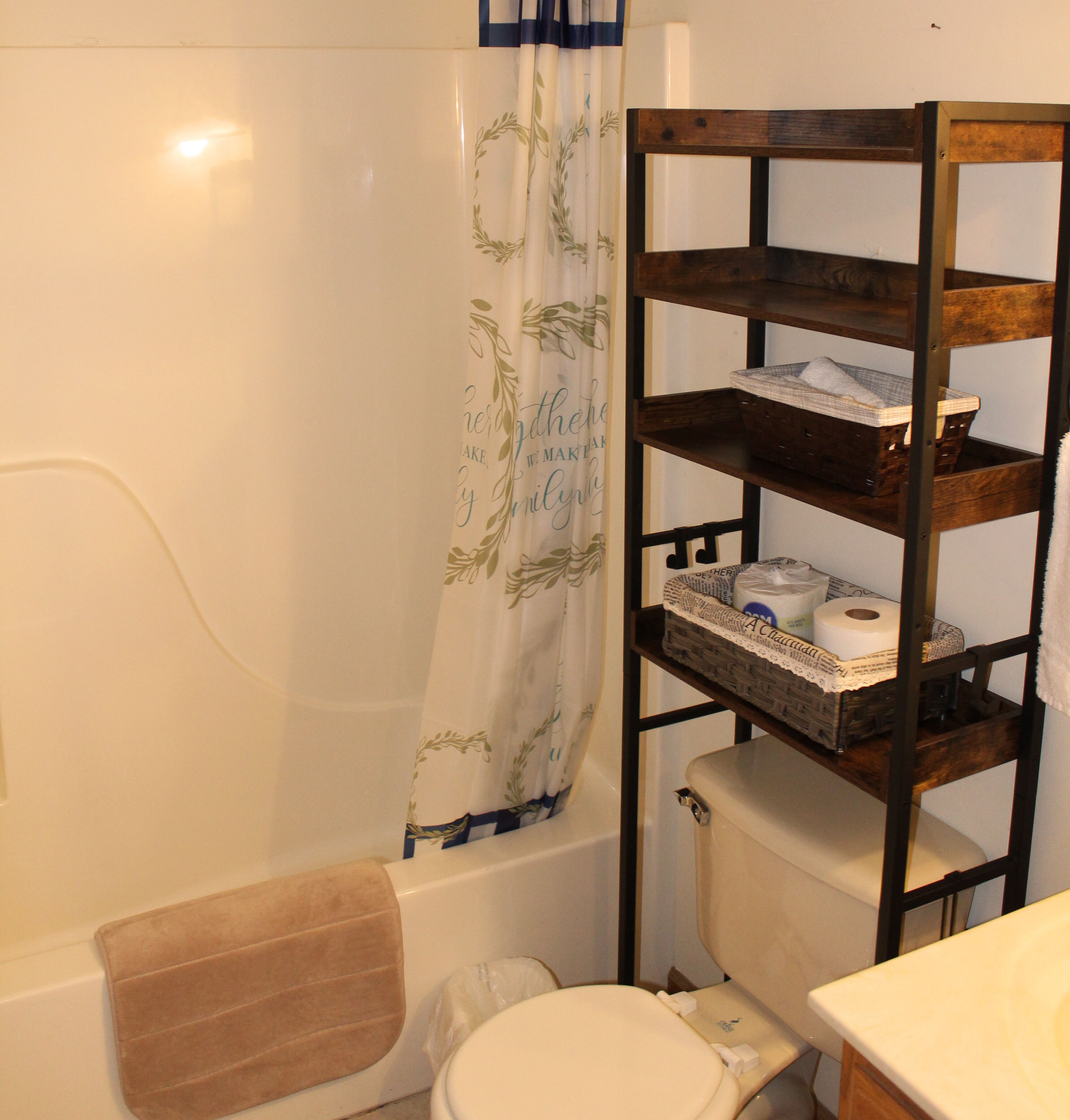 A bathroom with a bathtub, toilet, and a wooden shelf with toiletries.