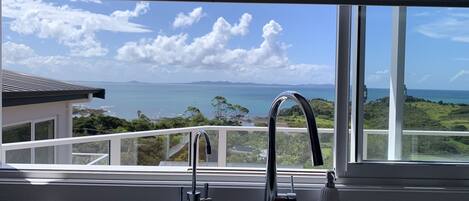 A kitchen with a modern faucet and a view of the ocean through large windows.