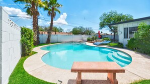 Un jardín trasero con piscina, palmeras y una mesa de patio.