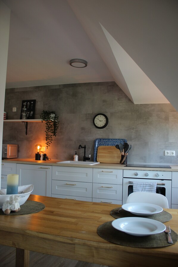 Une cuisine moderne avec une table en bois mise pour deux personnes, une plante suspendue et une horloge au mur.
