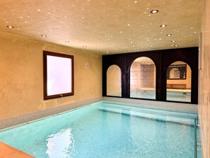 A swimming pool with a tiled border, a window with blinds, and a ceiling with recessed lighting.