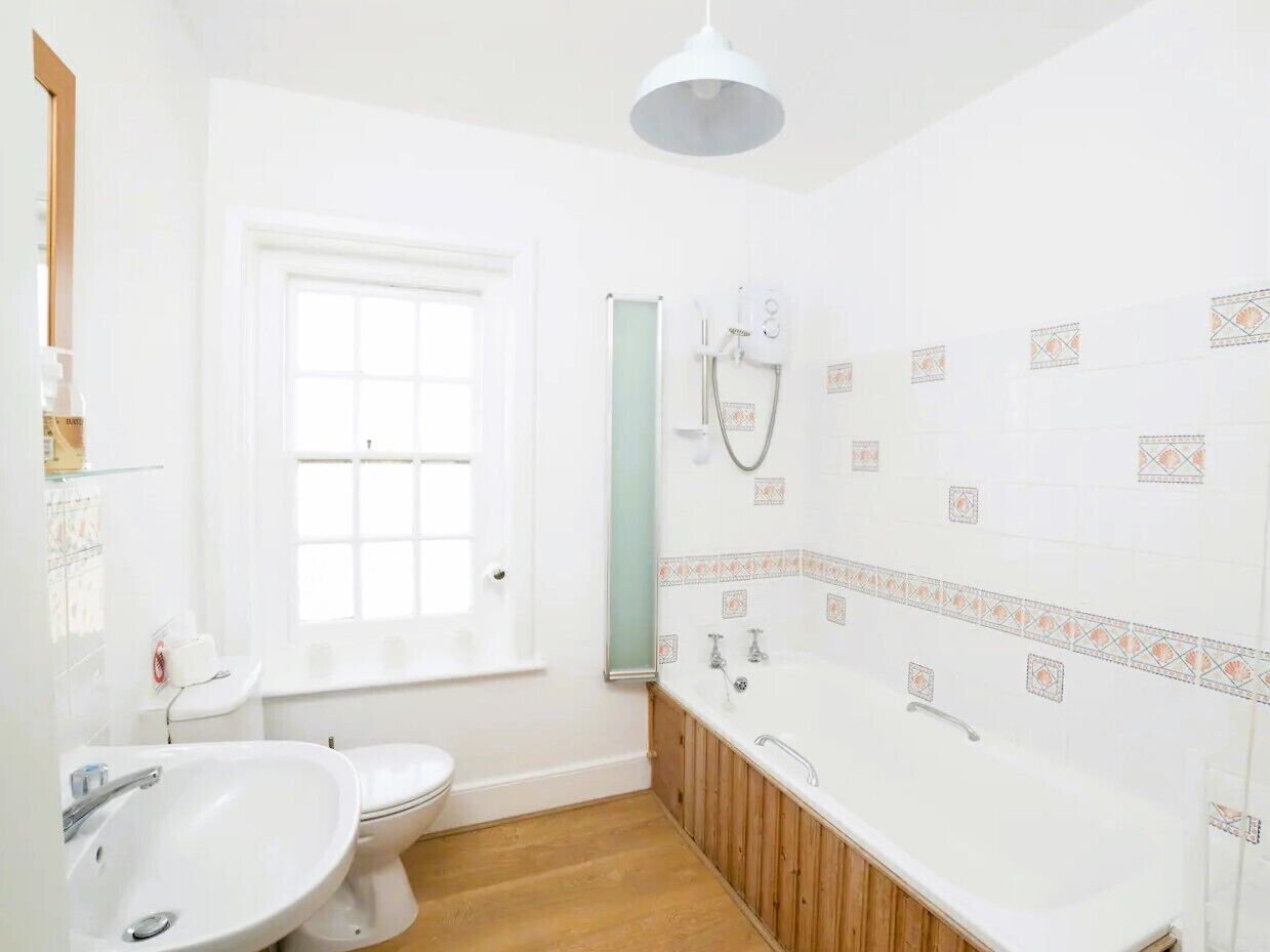 A bathroom with a white sink, toilet, and bathtub, a window, and a shower with a towel rack.