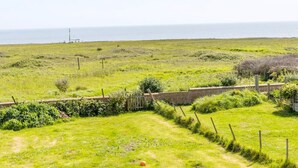 A coastal landscape with a grassy field, a stone wall, and a fence. - Coastguard Cottage (Atherfield)