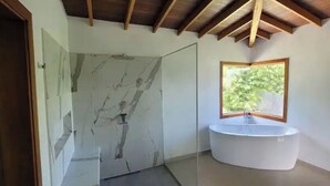 Ein Badezimmer mit Marmorwand, einem runden Waschbecken und einem Fenster mit Blick auf Grünflächen.