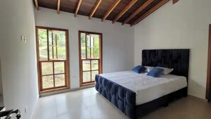 Ein Schlafzimmer mit einem Bett, zwei Fenstern und einer Holzbalkendecke.