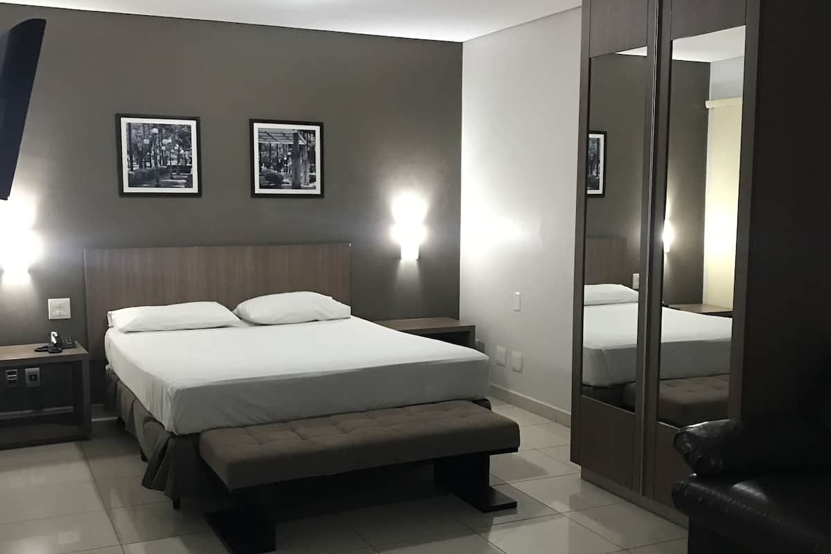 Une chambre moderne avec un grand lit, des tables de chevet, un banc et une armoire avec un miroir.