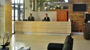 Un espace d’accueil avec un comptoir de réception en bois, deux réceptionnistes, un canapé noir et un téléviseur fixé au mur.