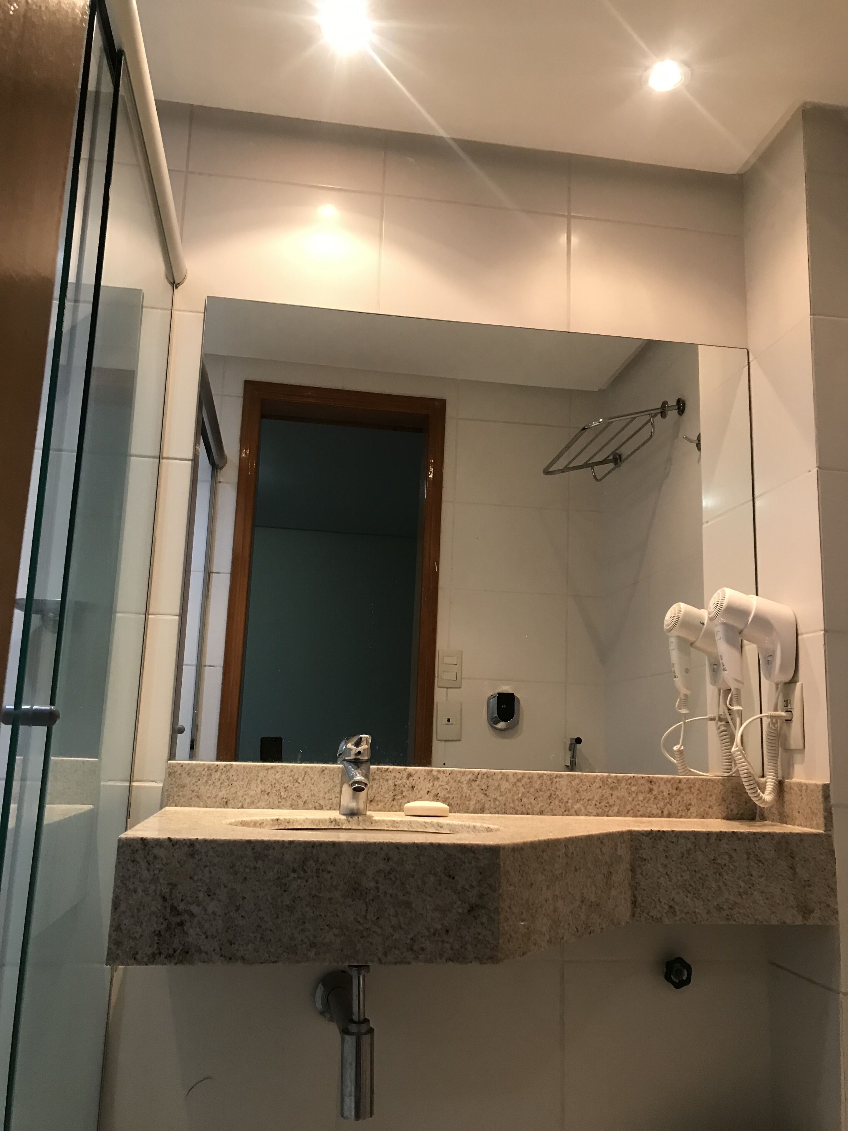 A bathroom with a granite countertop, a mirror, a sink, a handheld showerhead, and two hair dryers mounted on the wall.