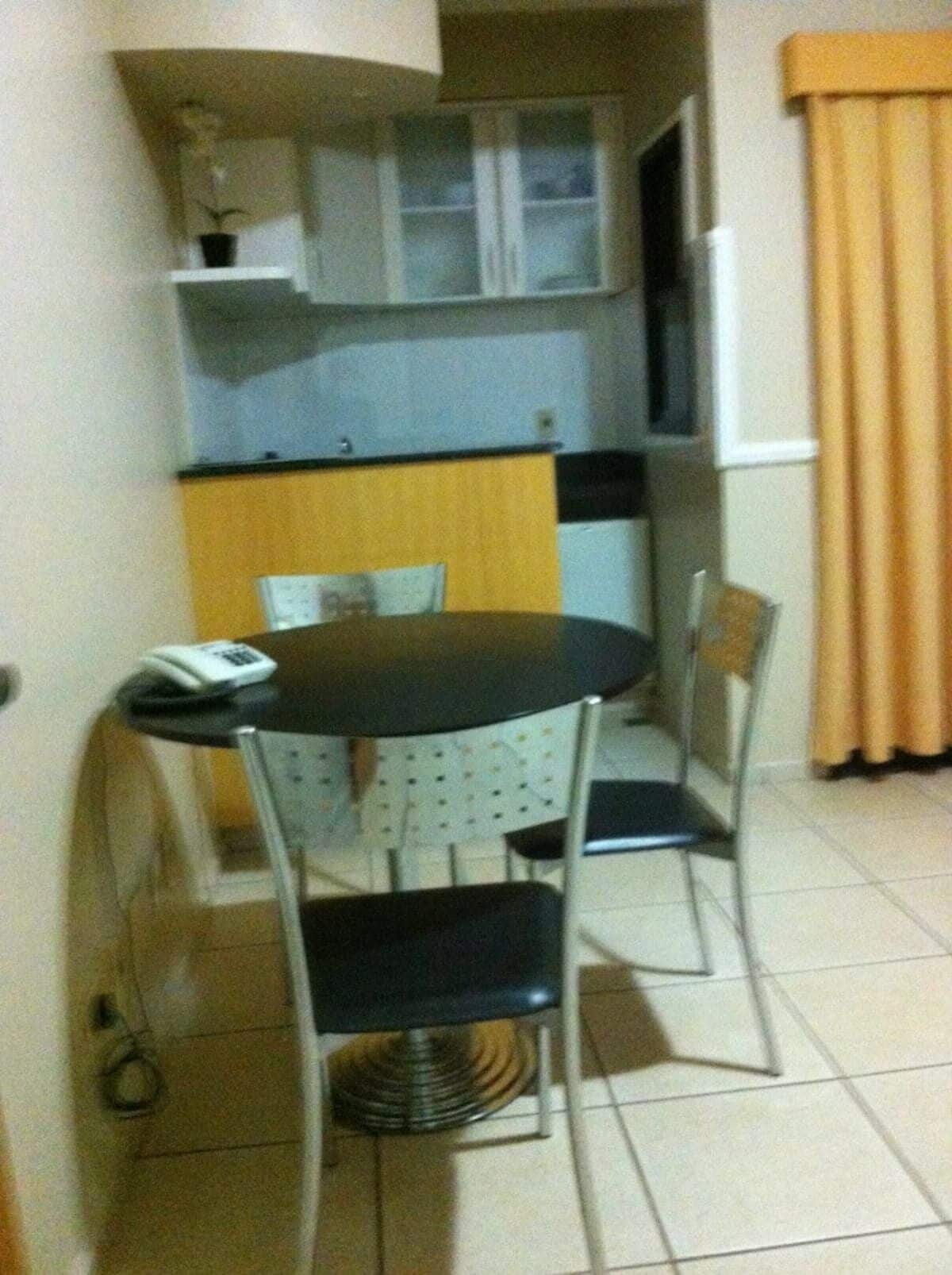 A small dining area with a round table and two chairs, a kitchen area with cabinets and a countertop, and a window with curtains.