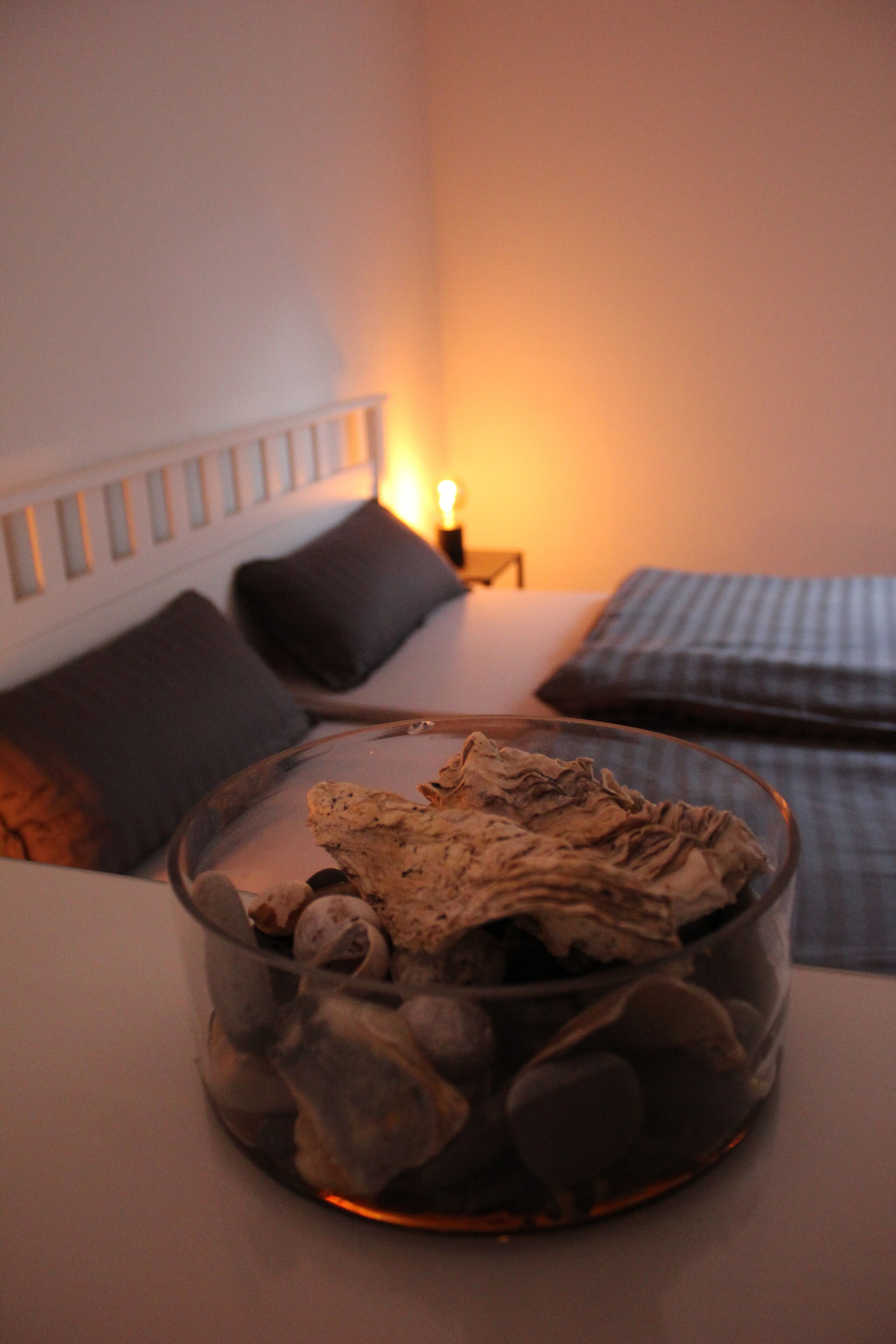 Ein Zimmer mit einem Bett, einem Nachttisch mit Lampe und einer Glasbowl mit Steinen.