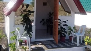 A small, single-room structure with a sloped roof, a door leading inside, and a small table with chairs outside.