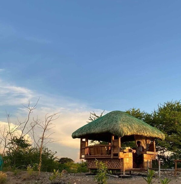 A wooden structure with a thatched roof, surrounded by trees and vegetation.