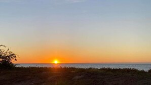 A sunset over a beach with a clear sky and a visible moon.