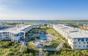 A modern hotel with multiple buildings, a central pool area, and a view of the sea.