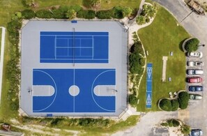 An aerial view of a sports complex with two tennis courts, a parking area, and surrounding greenery.