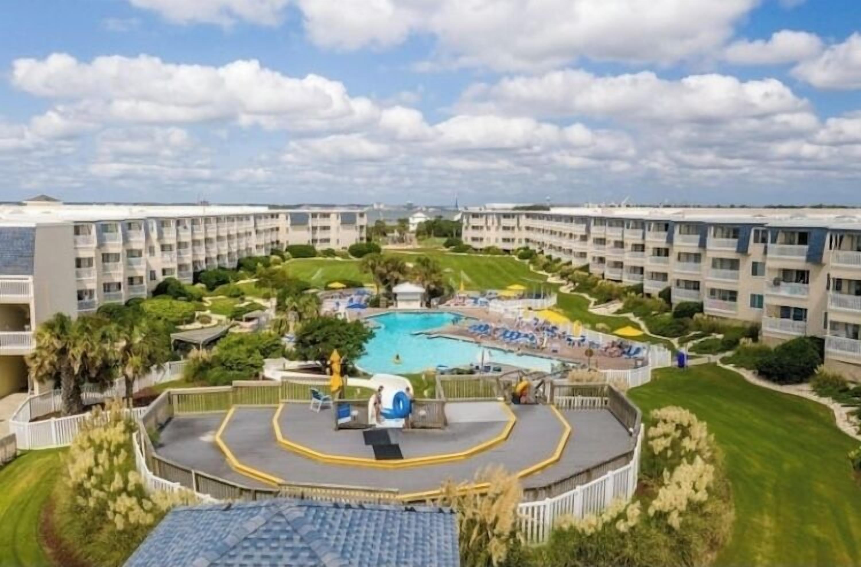 A resort with a central pool, multiple balconies, and well-maintained lawns.