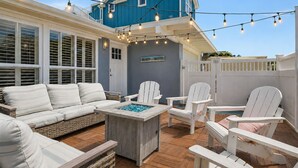 Une terrasse extérieure avec un canapé blanc, des fauteuils Adirondack, une table en bois et des guirlandes lumineuses.