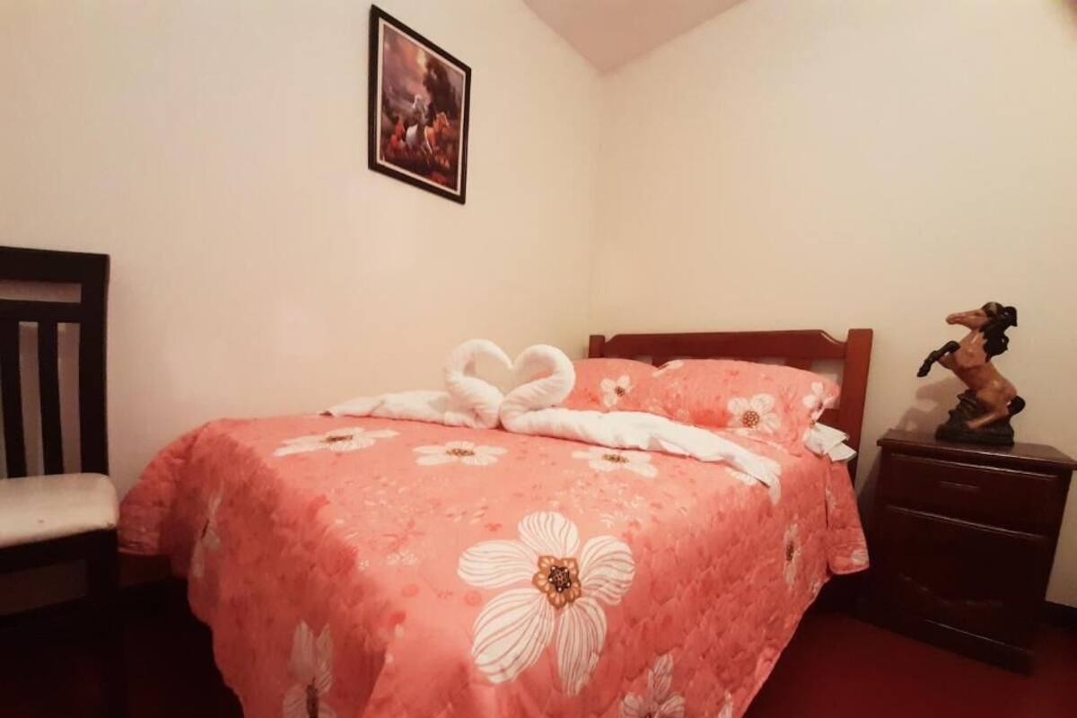 A bedroom with a bed, a chair, a nightstand, and a wall-mounted picture.