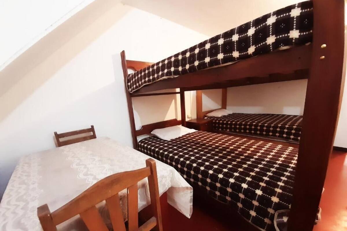 A dormitory room with bunk beds, a wooden desk, and a chair.
