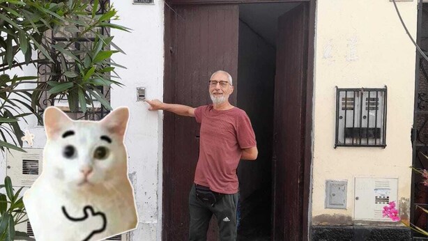 Un hombre de pie frente a un edificio con una puerta, un ventanal y una planta pequeña.